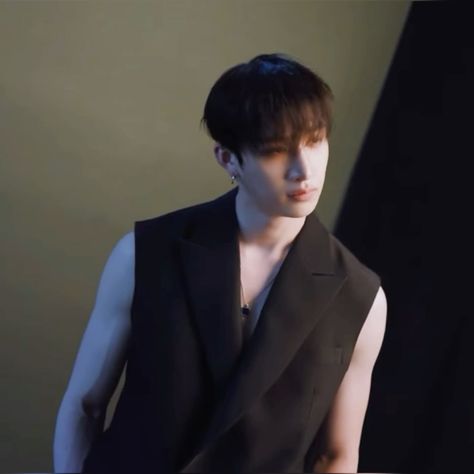 This  contain an  image of Bangchan in a black vest standing next to a wall