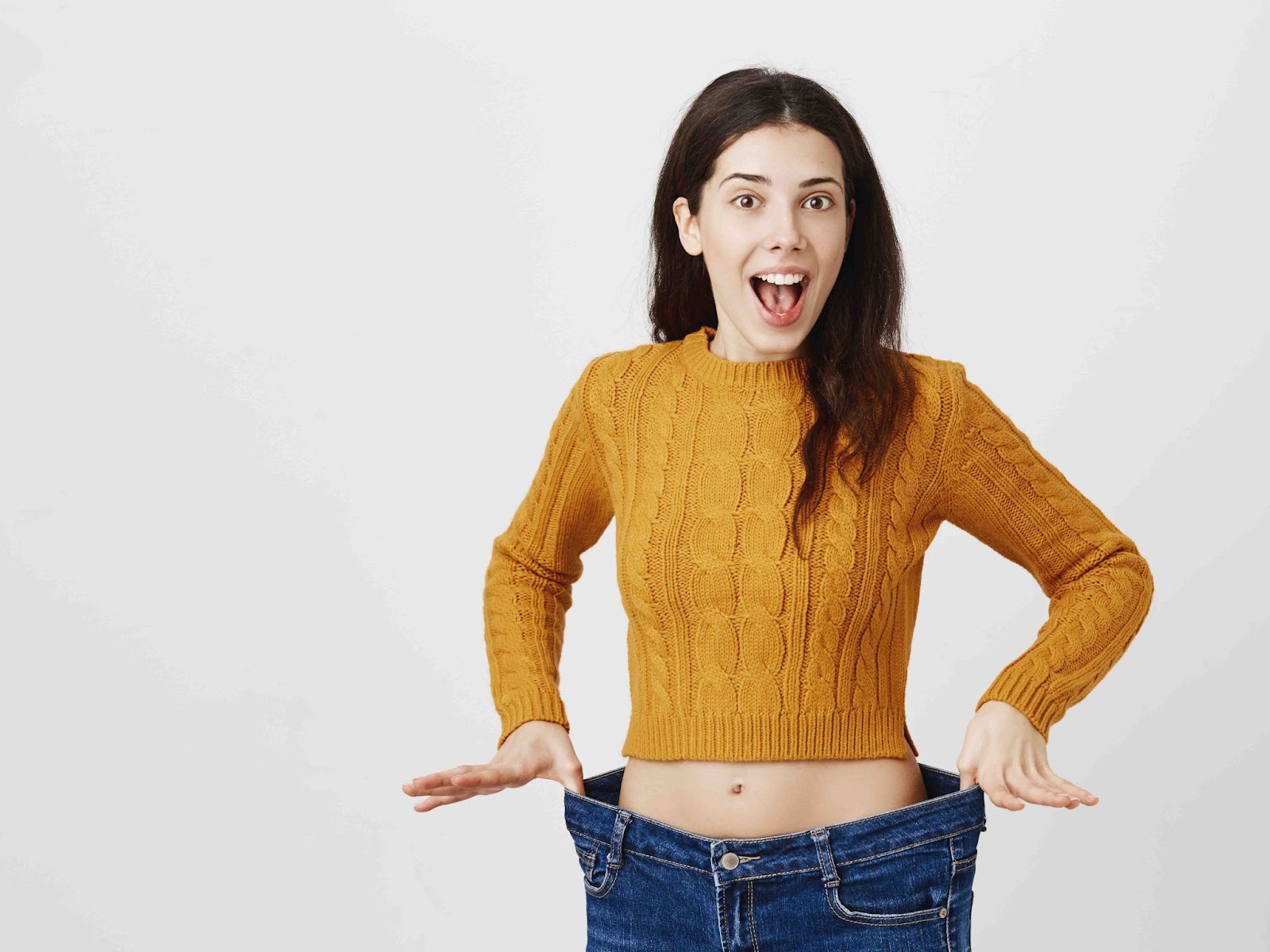 Woman excitedly showing her oversized jeans, representing the success of exercise for weight loss and achieving fitness goals