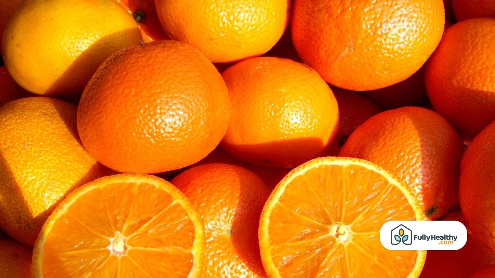 Whole and halved oranges stacked under sunlight with vibrant orange color