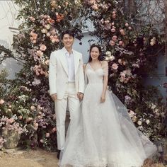 This may contain: a man and woman standing in front of a floral arch