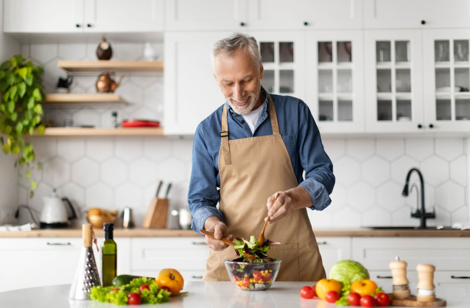 A senior man smiling while preparing a healthy salad in his kitchen as part of the keto diet.