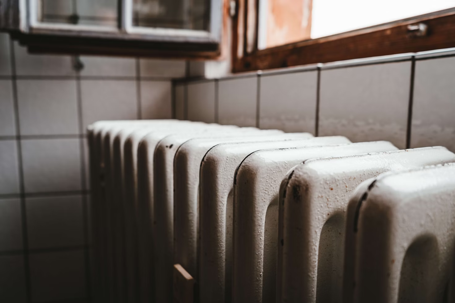 Close-up of an old radiator in a tiled room, showing the metal fins that distribute heat throughout the space