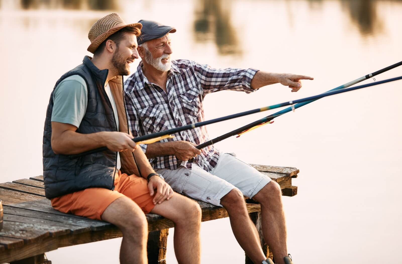 A senior fisherman and their child sit on a dock and fish together.