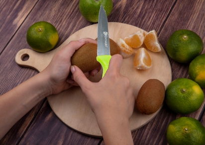 Seseorang sedang memotong kiwi dengan pisau, menyiapkan buah segar untuk dinikmati.