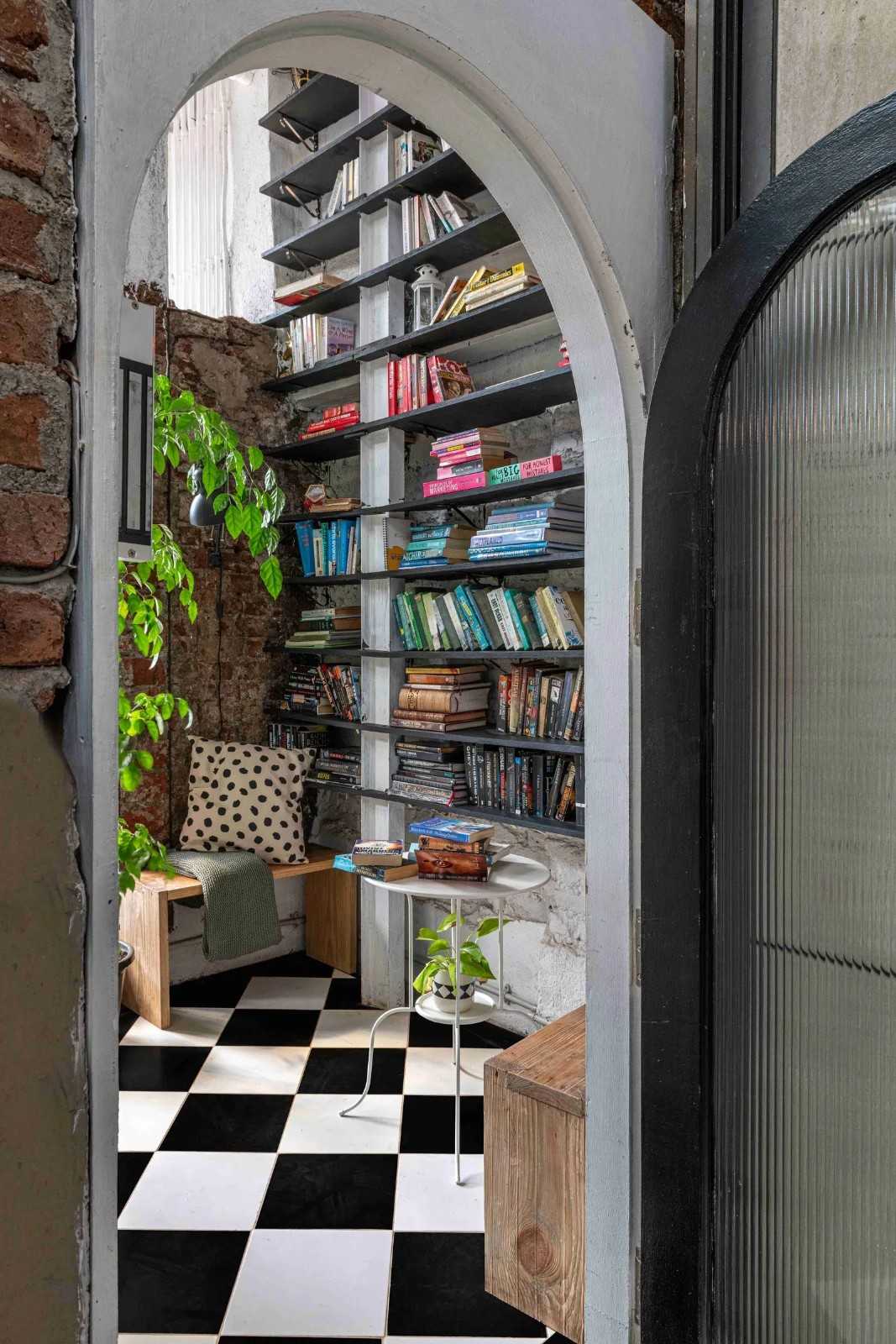 A cozy reading nook at the workspace with black-and-white checkered flooring, featuring a tall bookshelf packed with books in the background.