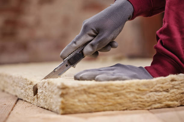 Worker uses protective safety gear to cut the fiberglass insulation.