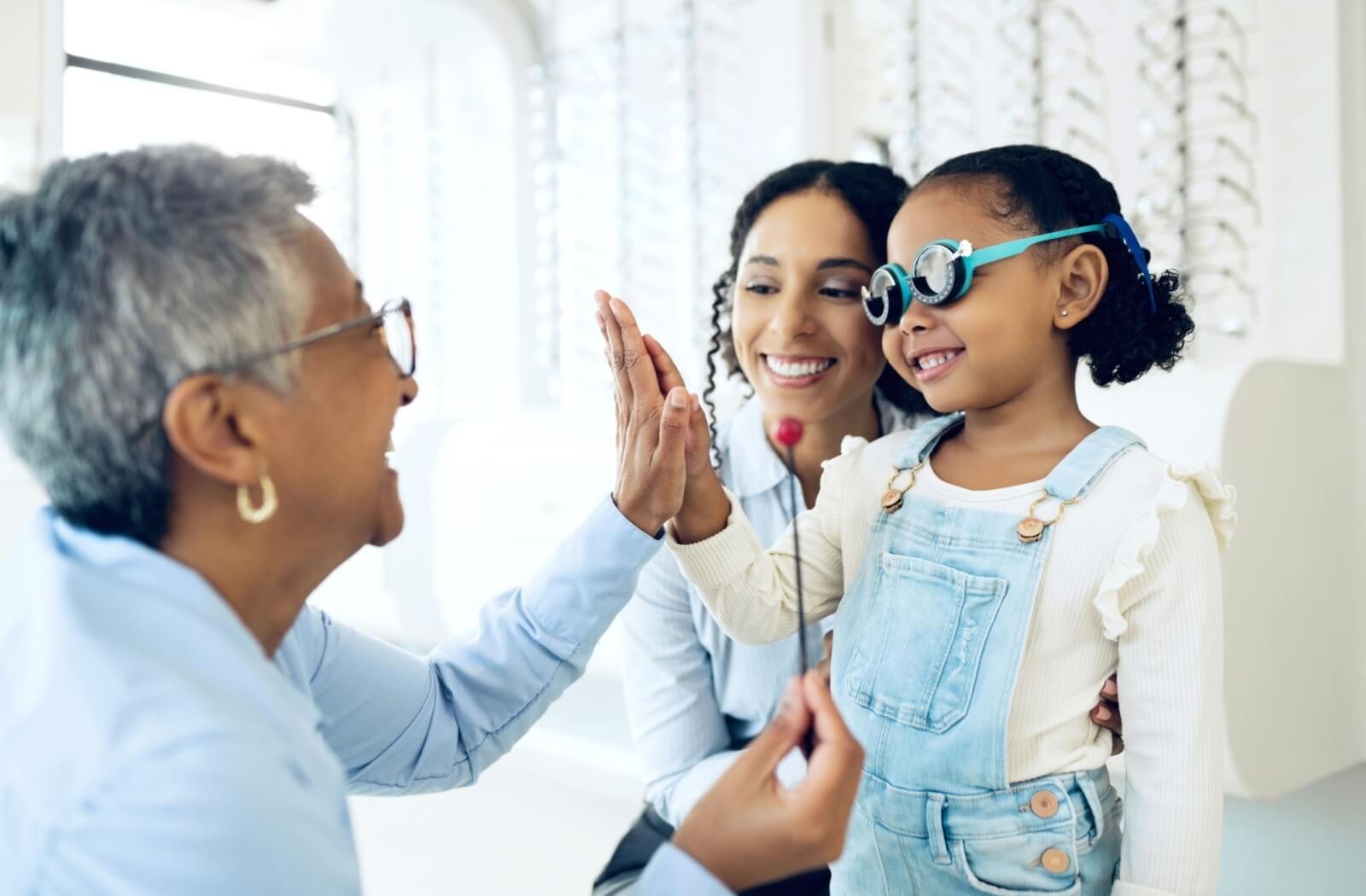 An optometrist high-fives their young patient after an eye exam with their parent.