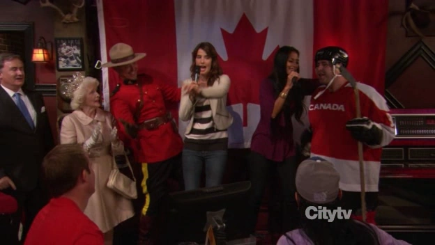 Robin y su amiga Glitter cantando con un jugador de hockey, un guardia montada, una señora vestida de la reina de Inglaterra y una bandera de Canadá.