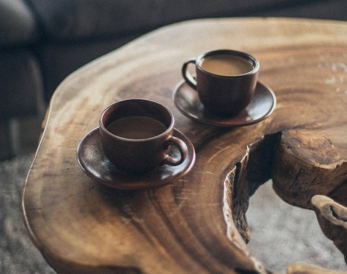 Two dark coffee cups on saucers sit on a reclaimed wooden table