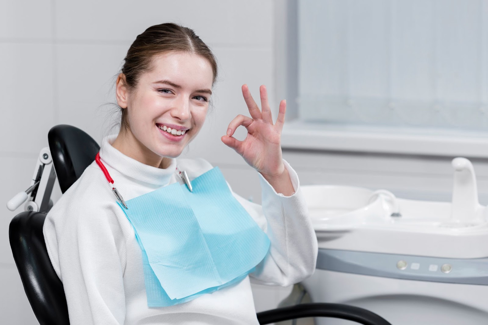 Happy female patient giving an OK sign after a successful dental treatment at the clinic