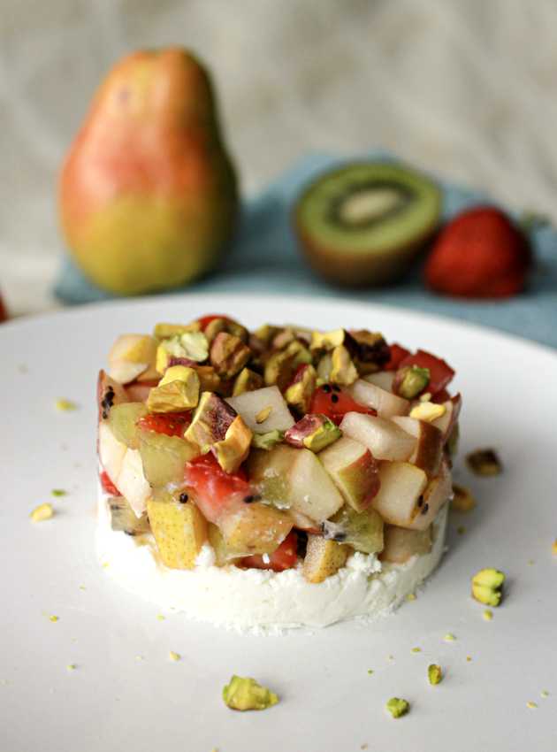 Fruit tartare made with diced pear, kiwi, strawberry, and pistachios on a white plate.