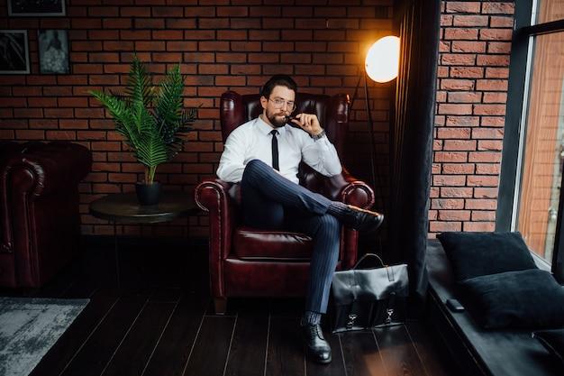 Millionaire man resting and relaxing while sitting on sofa in luxury room. Handsome man smoking cigar or iqos.