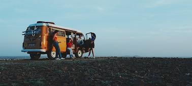 Example image of four men and women chatting around an orange campervan