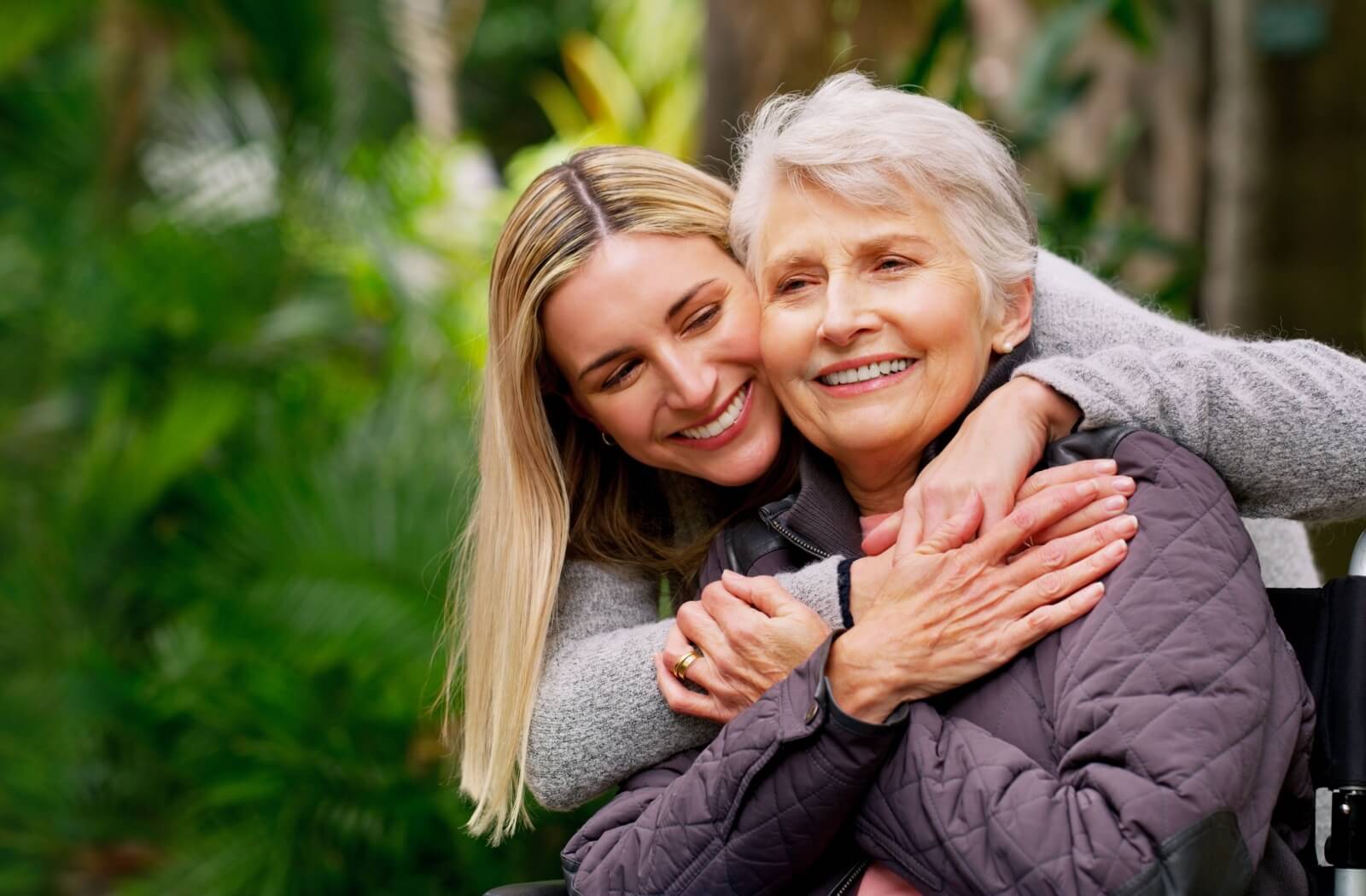 A happy adult child and their senior parent hugging and enjoying a visit in the older adult's assisted living community.