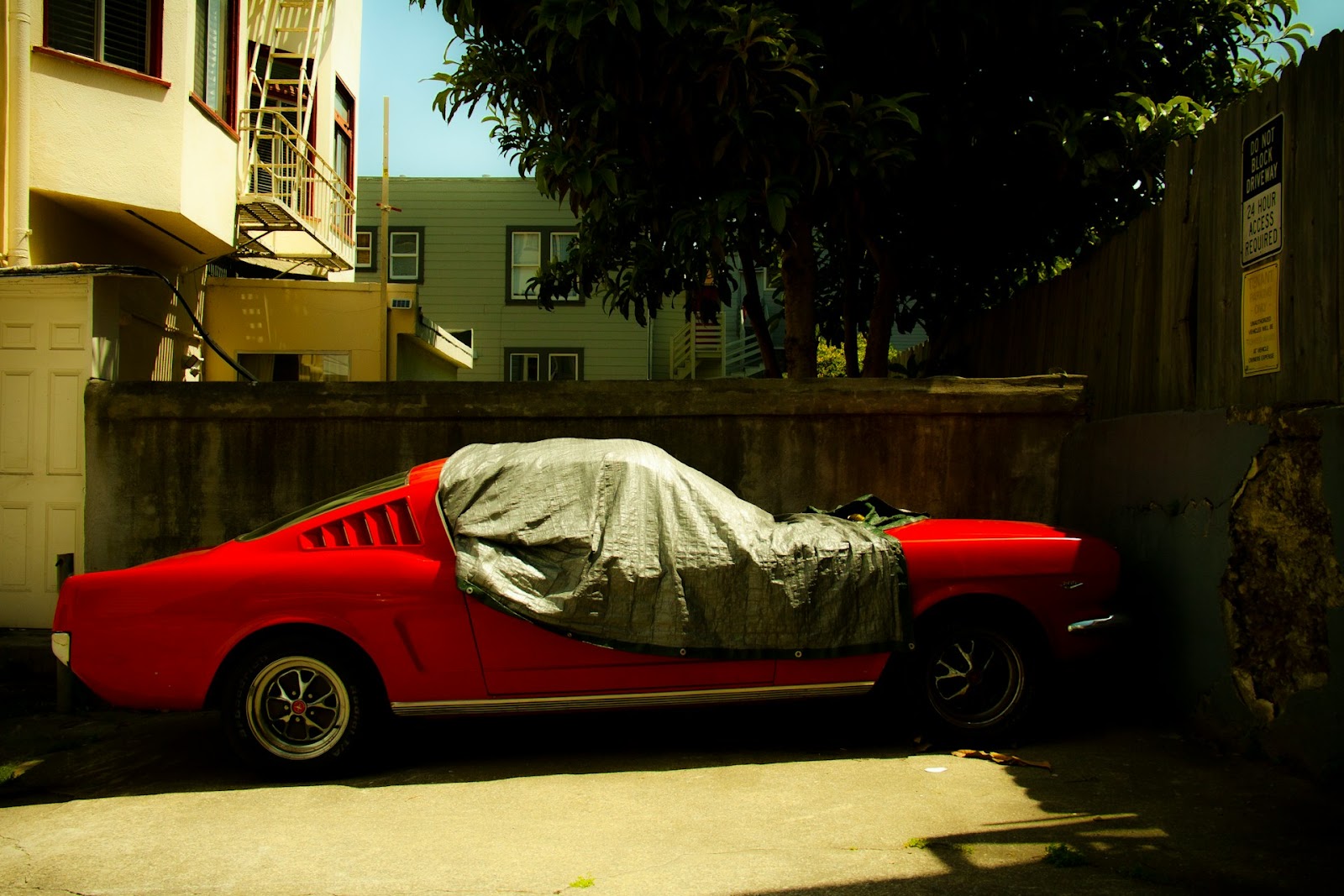 the car is covered from the sun in the yard