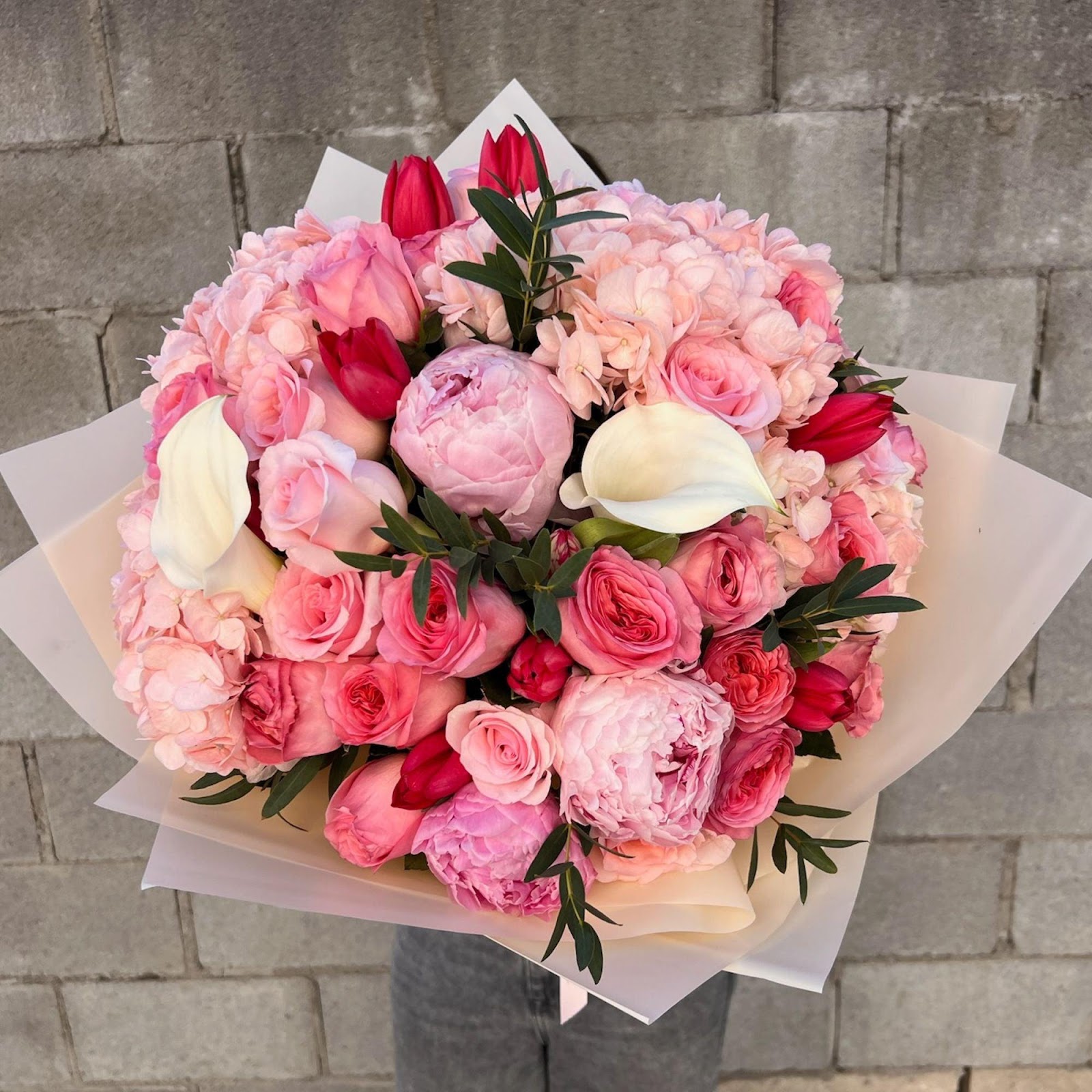 A stunning floral arrangement showcasing peonies, tulips, garden roses, calla lilies, hydrangea, and eucalyptus, creating a lush and vibrant display of colors and textures.