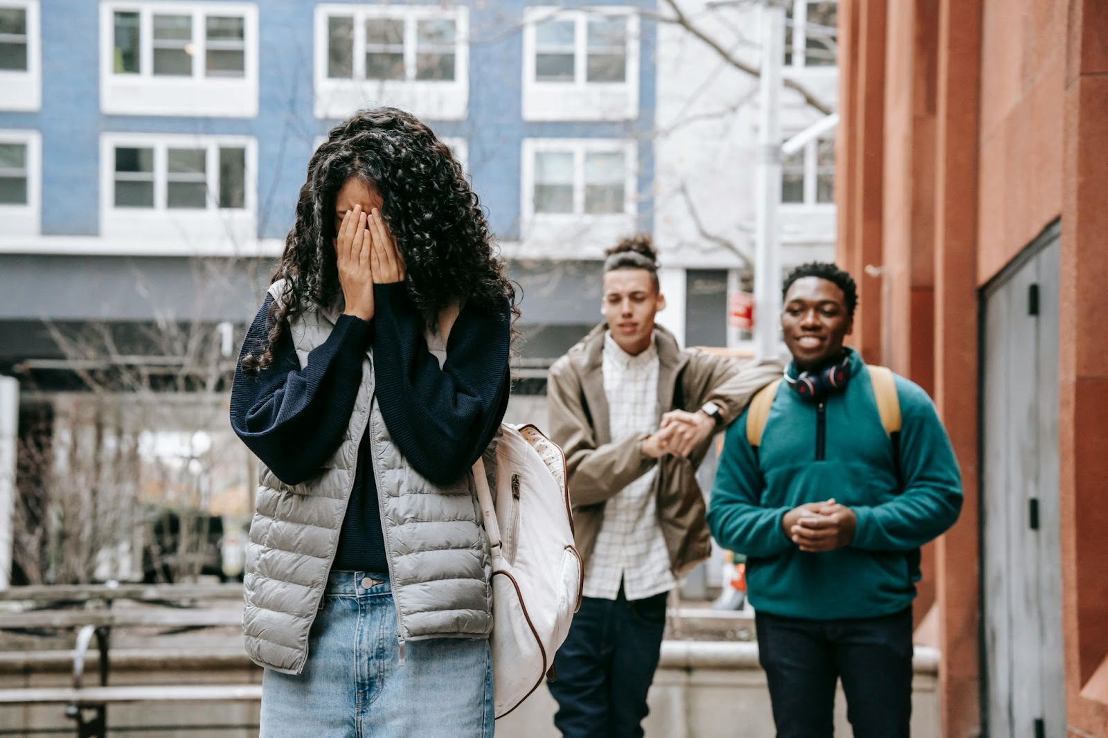 A tudent walking away from two bullies with her hands covering her face in shame