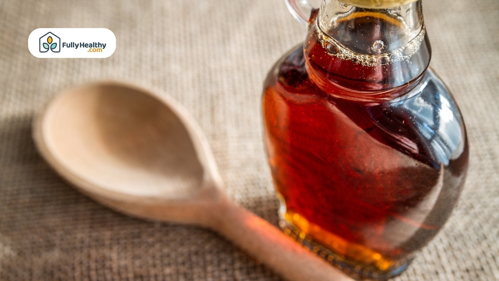 Maple syrup bottle beside wooden spoon on burlap background