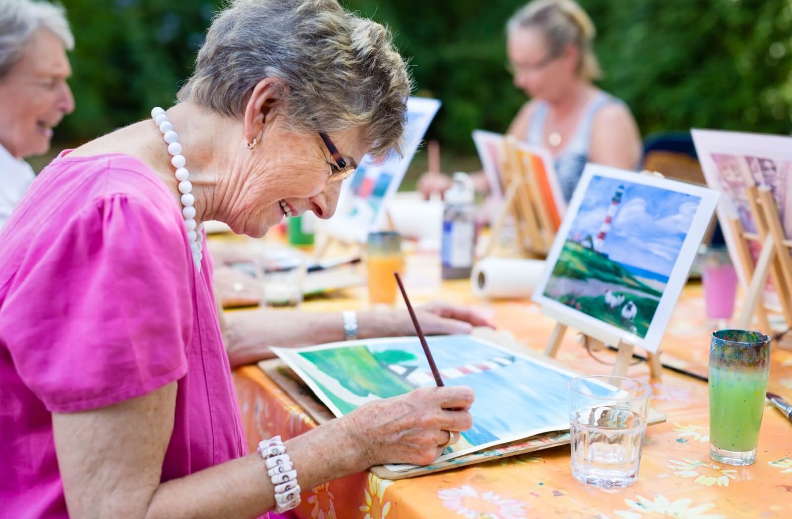 A group of happy seniors participate in a group art class outdoors in their independent senior living community.