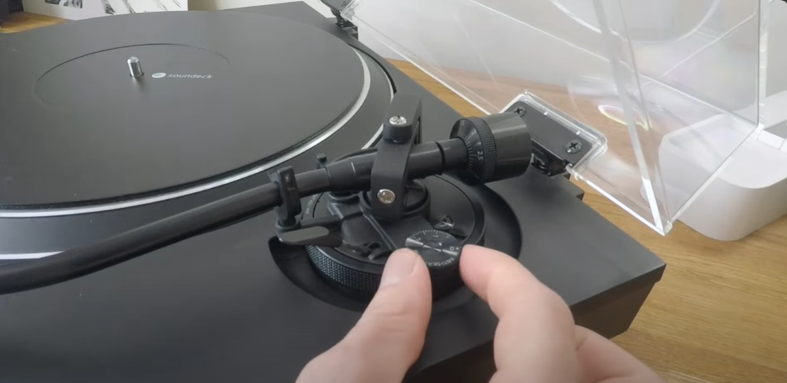 Hands adjusting the anti-skate control on a turntable's tonearm.