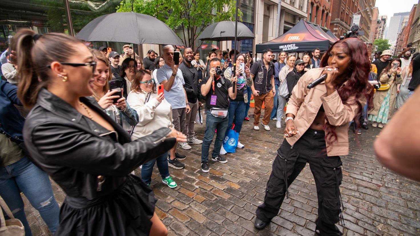 A person in a black jacket and black pants performing on a street with a crowd of people Description automatically generated