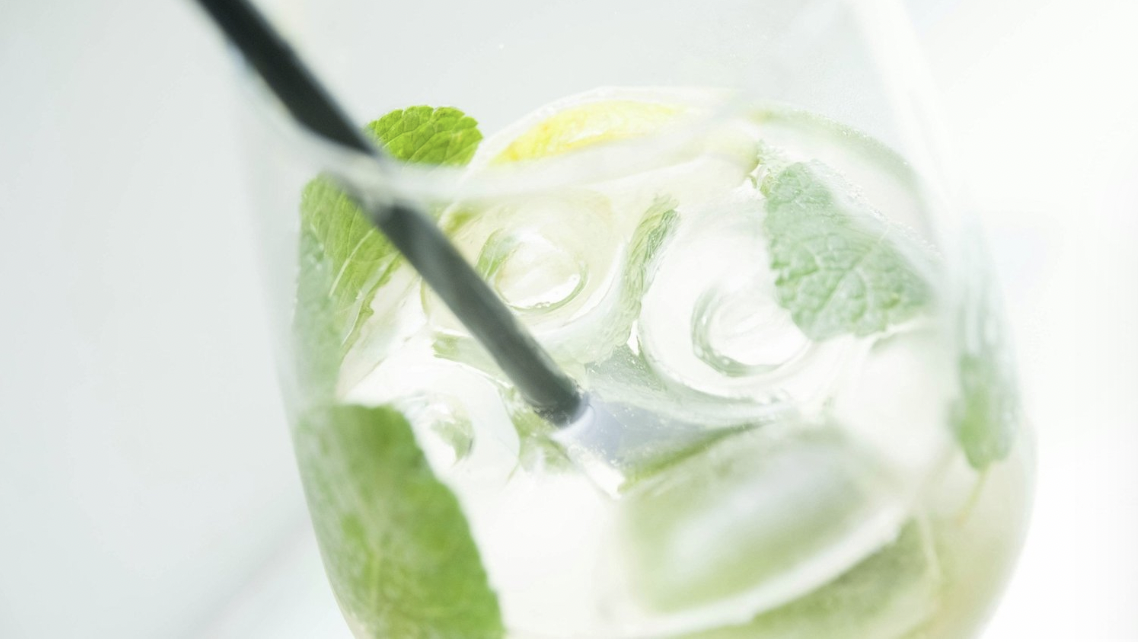A Hugo cocktail fills a wine glass with ice, mint, lemon, and a black straw