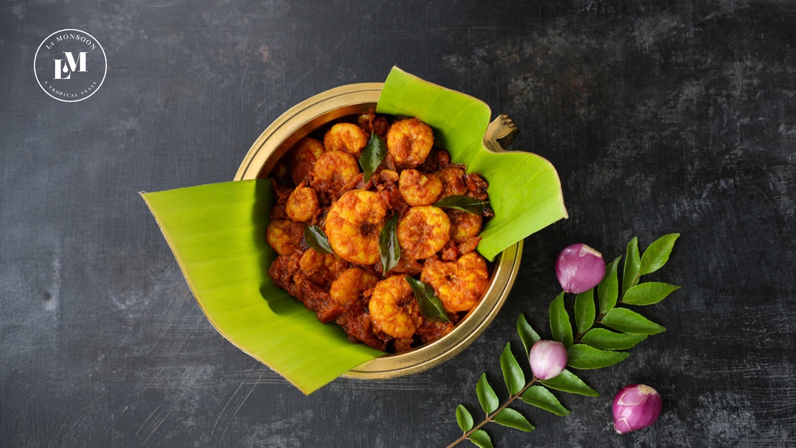 A vibrant bowl of spicy prawn fry garnished with curry leaves, surrounded by banana leaves on a dark background.