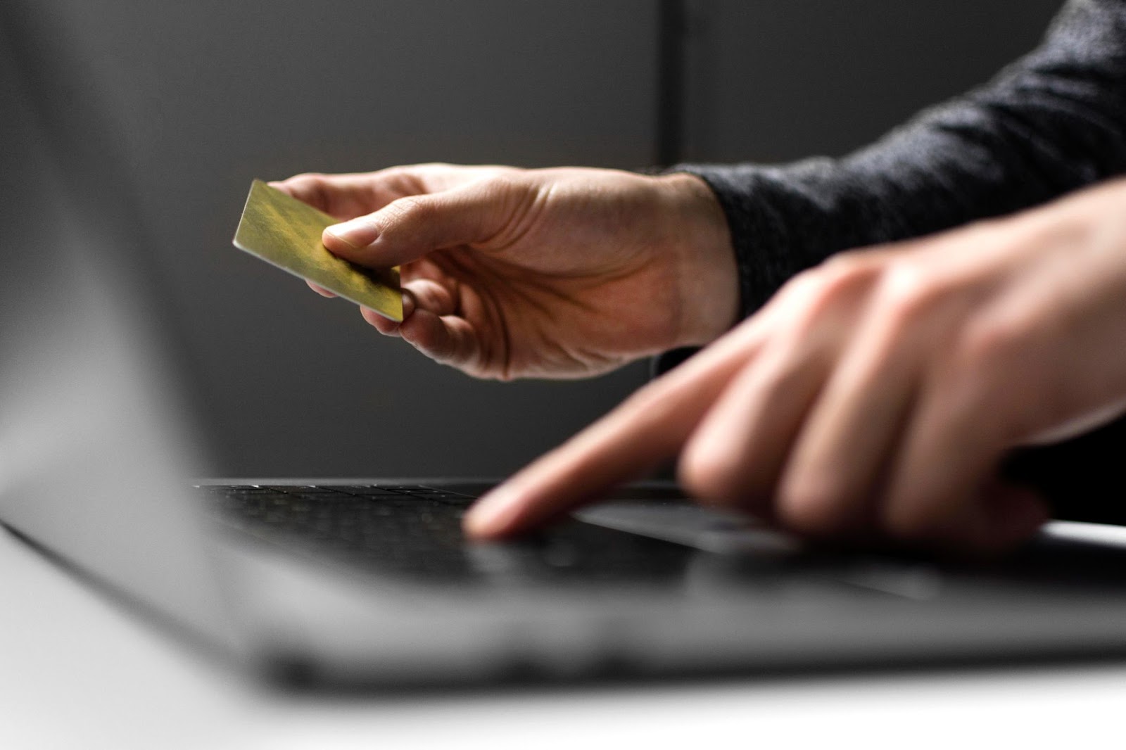 Hand extending a credit card towards a laptop