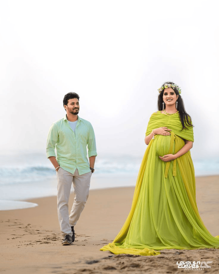 Pregnant couple standing and smiling with floating flower tiara during beach maternity photoshoot