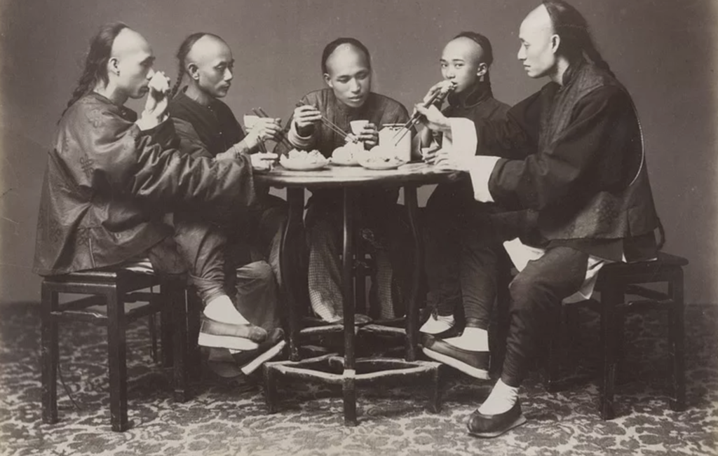 A white and black photo of five Han Chinese men sitting around a table, enjoying dinner.