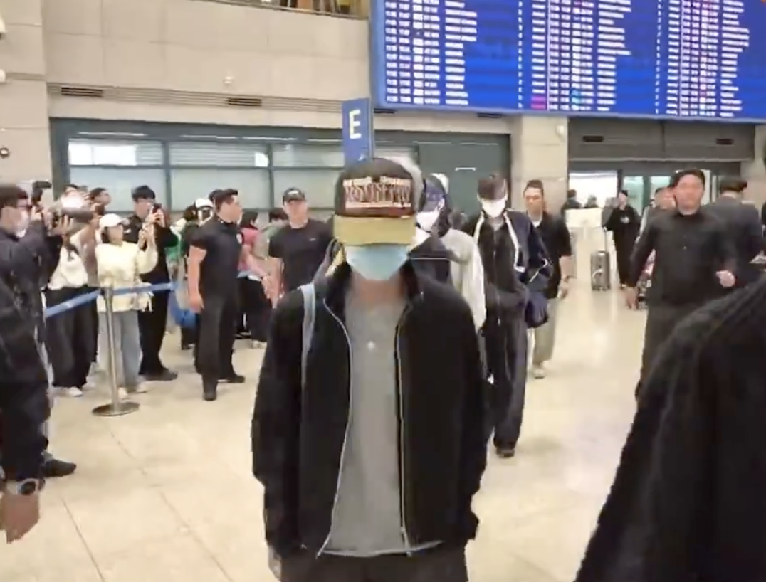 A photo of RIIZE Seunghan at the airport wearing a black jacket and a cap putting  his hand in his pocket