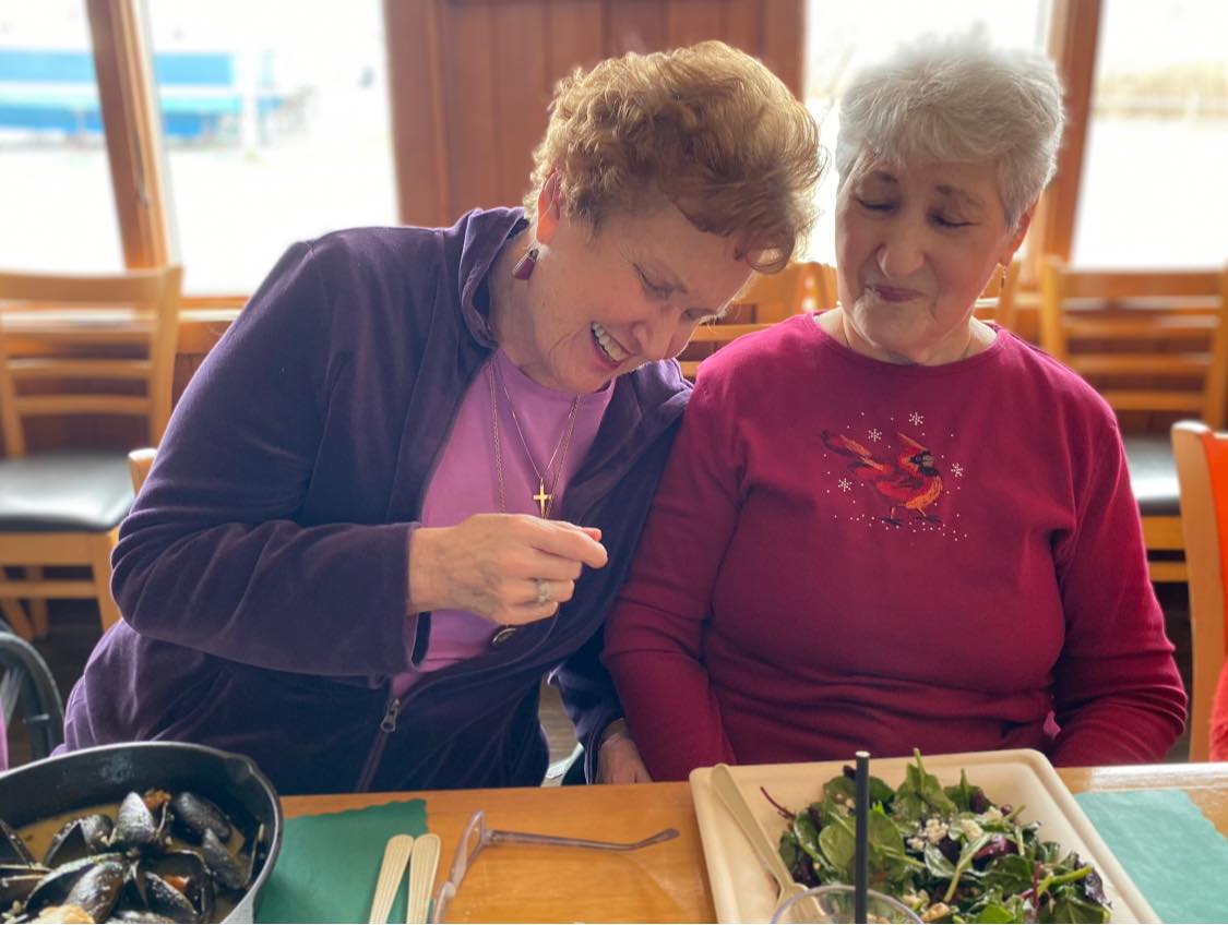 Two women smiling and rocking next to one another while eating a salad and oysters