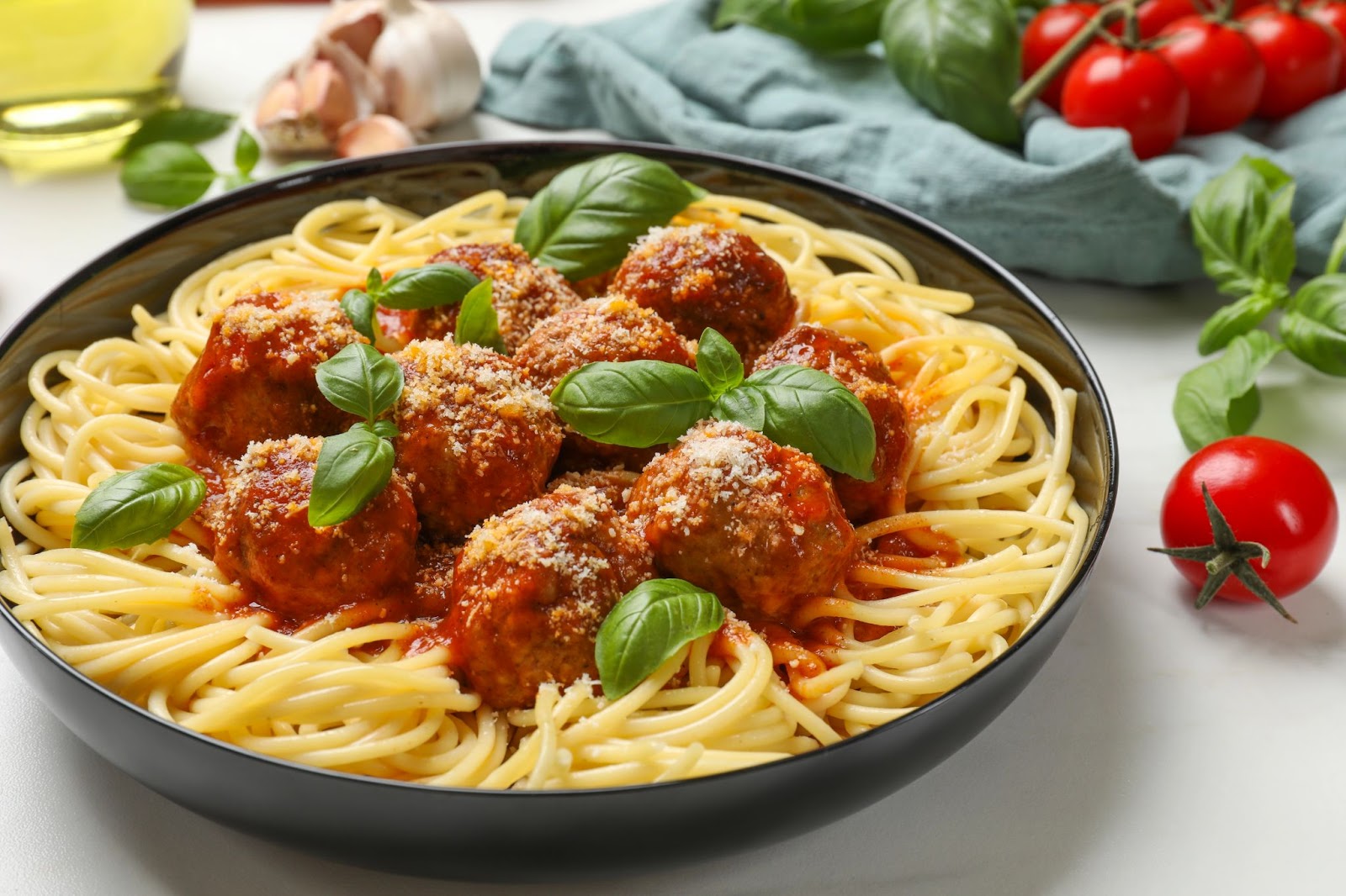 Spaghetti and meatballs with basil garnish plated near tomatoes and basil