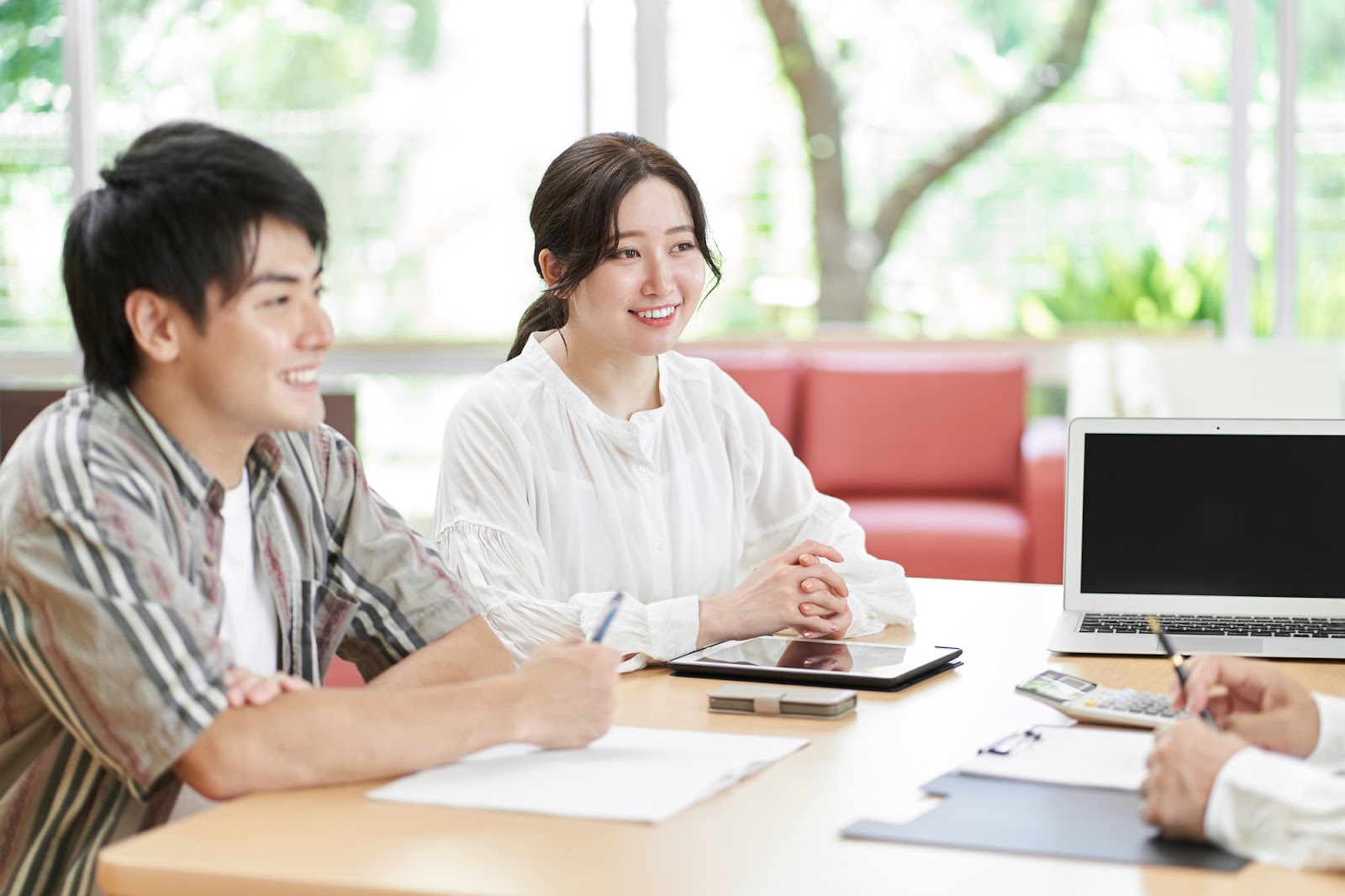 住宅ローンや二世帯住宅の間取りの相談をする若い夫婦と住宅会社の担当者｜家づくりの打ち合わせ風景