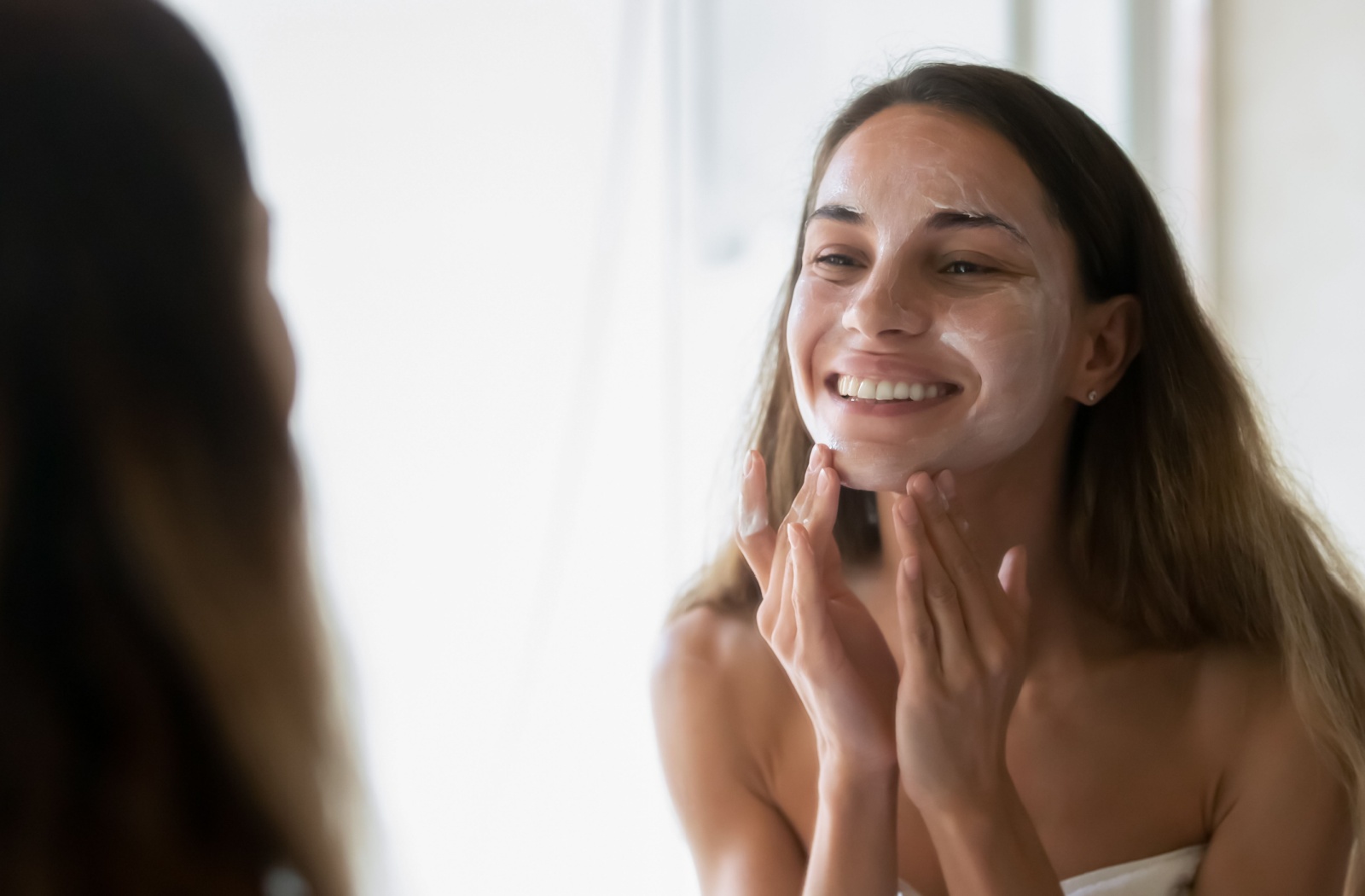 An adult applies sun protection in the morning while looking in a bathroom mirror.