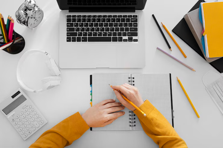 Top view of a hand writing on a notebook with a laptop in front