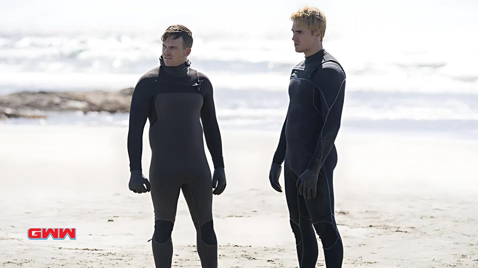 Lachlan Quarmby and Simon Arblaster in wetsuits on a beach, discussing, "Tracker" show.