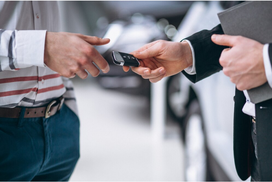 A car salesman hands over car keys to a customer in a dealership