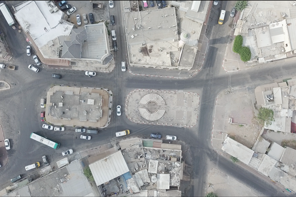 An aerial shot of Palmach Square with a circular monument at the center, surrounded by dusty buildings.