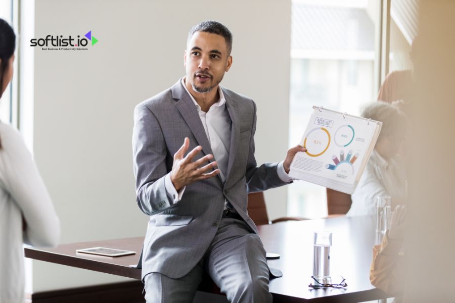 Man in suit presenting with a chart while sitting on a desk