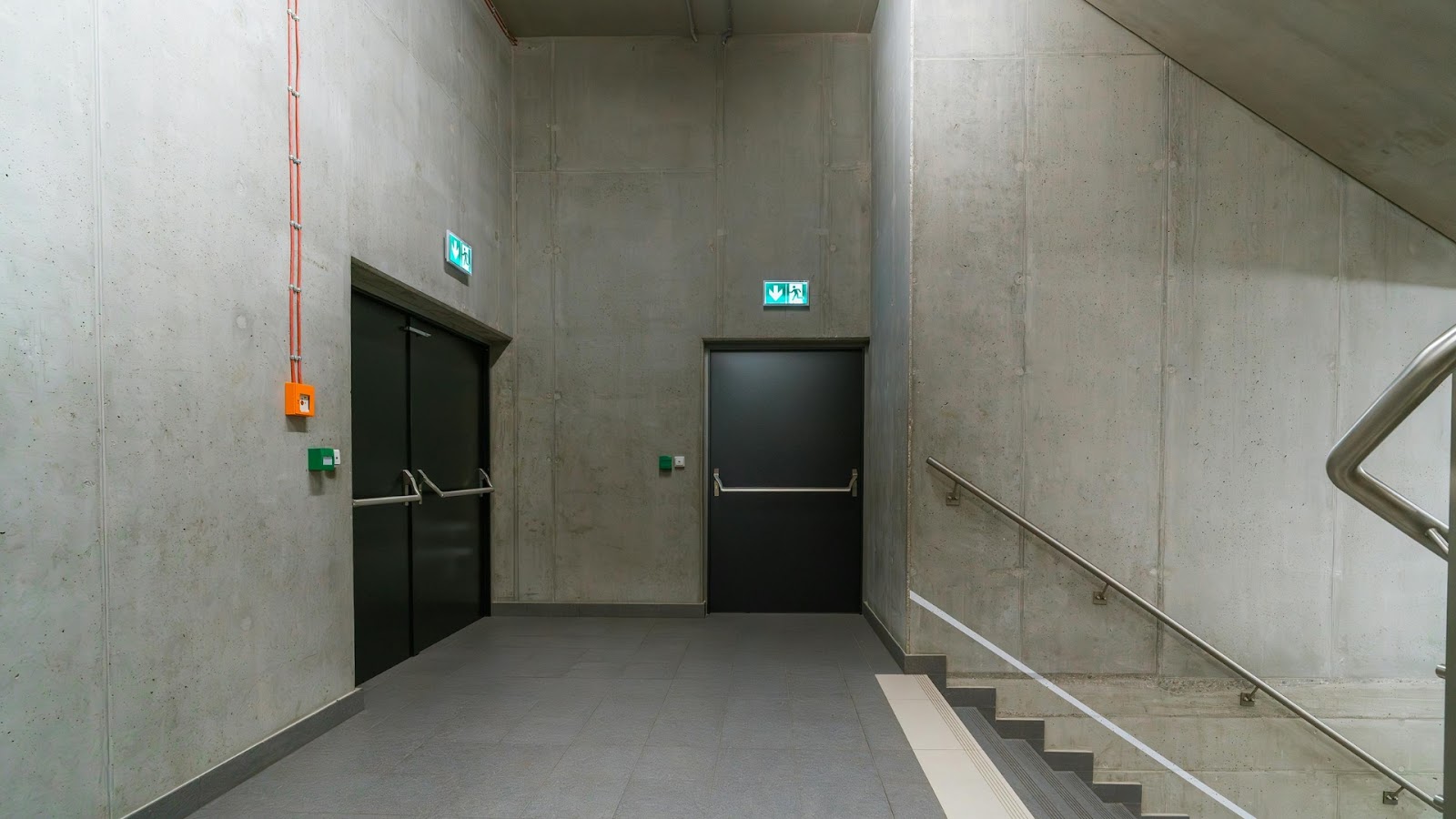 Concrete-walled stairwell with clearly marked emergency exit area featuring double and single doors with push bars and safety lighting for quick evacuation.