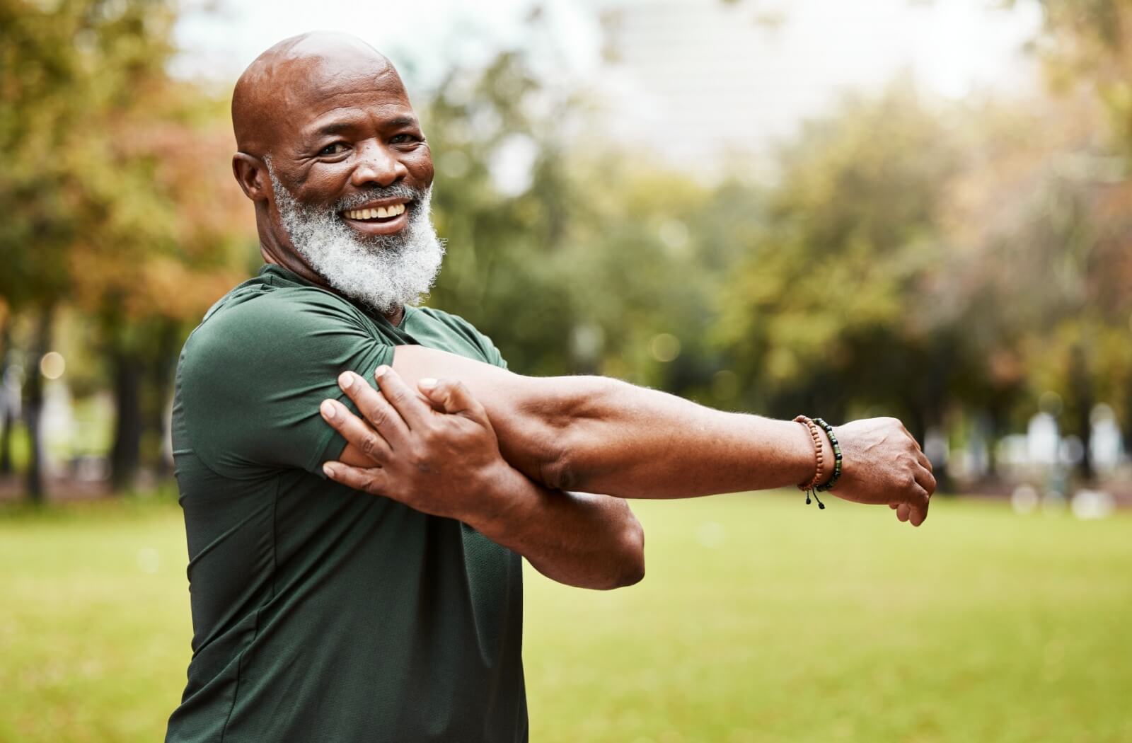 An older adult performing a shoulder stretch outside while smiling.