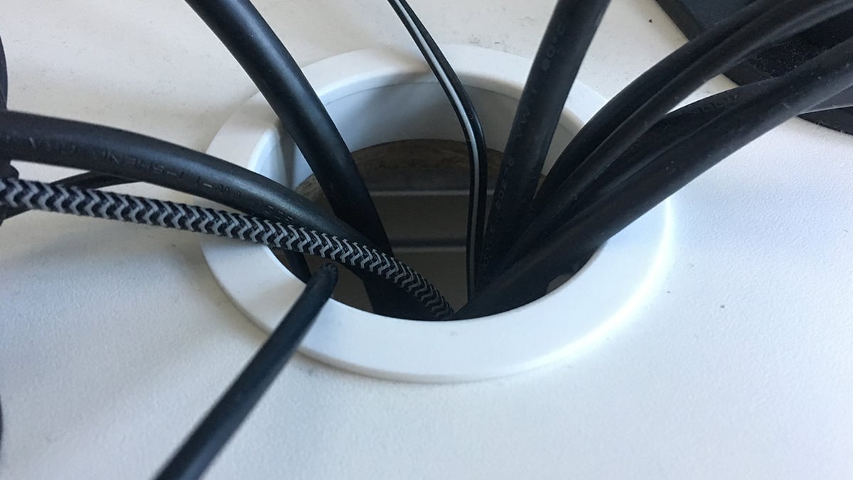 A work desk with multiple cables fed through a grommet hole.