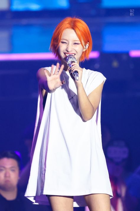 This contains a picture of Soyeon  with orange hair holding a microphone in front of an audience at a concert