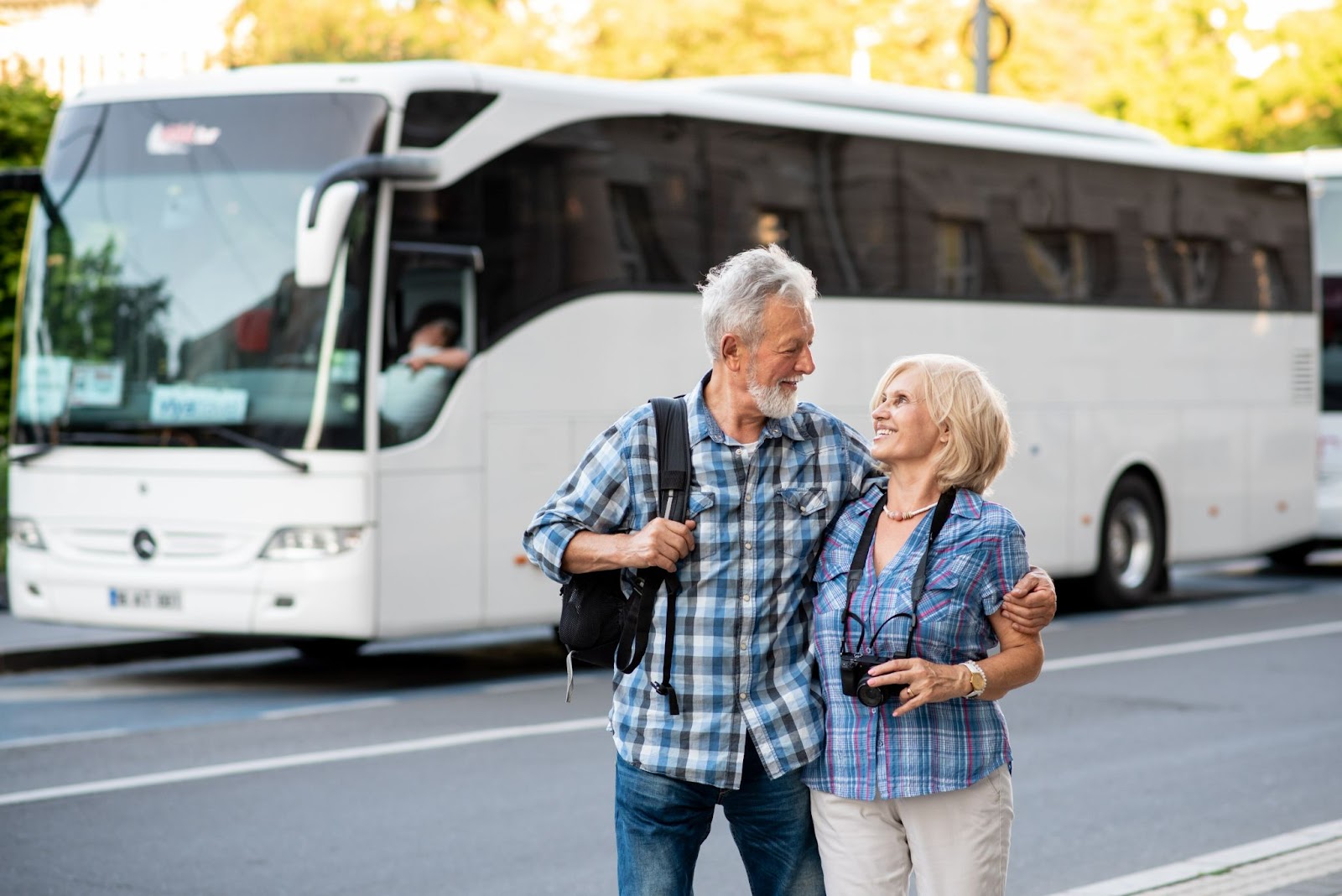 Casal de idade abraçado em frente a um ônibus branco.