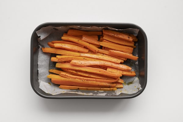 Raw sweet potato sticks seasoned with pepper and oil, arranged on parchment paper in a black air fryer tray