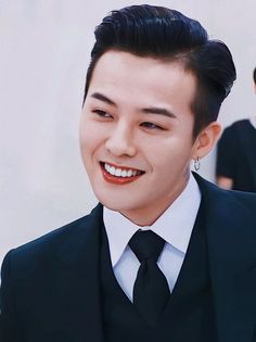 This contains an image of G-Dragon putting on suit smiling