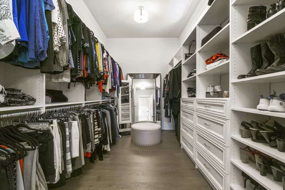 Primary walk-in closet with white built-in shelves, a round ottoman, and a full-length mirror.