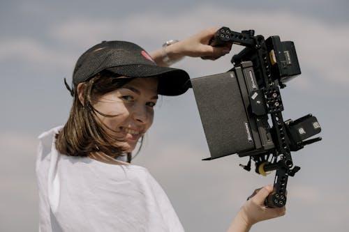 Free Smiling woman holding a camera rig in an outdoor setting, showcasing filmmaking in action. Stock Photo