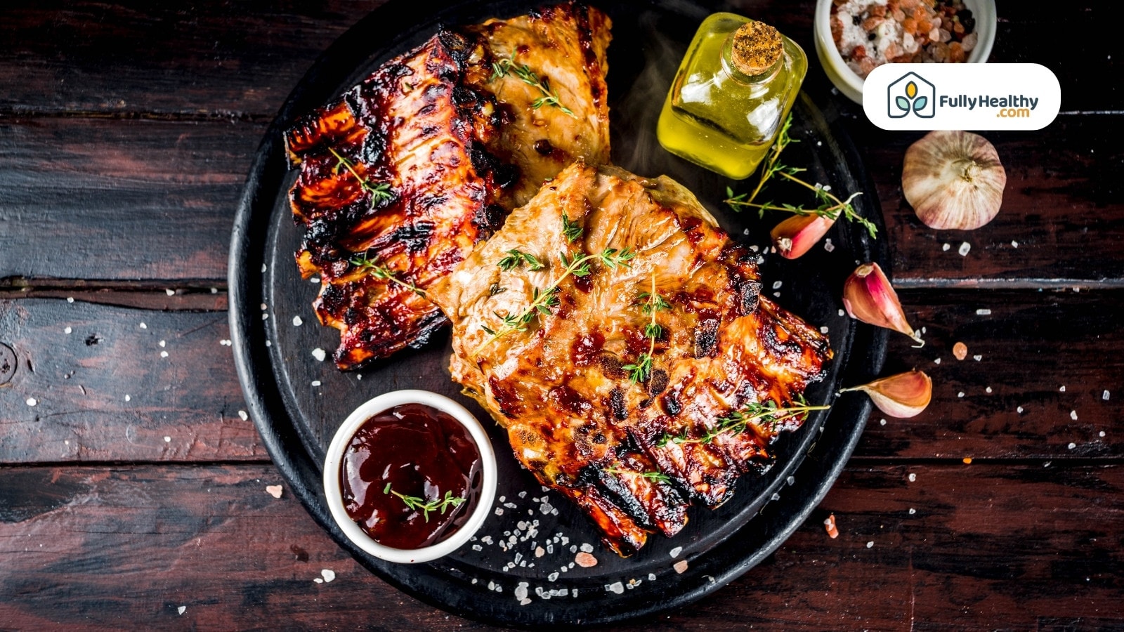 Grilled ribs on black plate with sauce and garlic cloves nearby